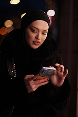 Image showing uropean Muslim Hijabi Business Lady checking her phone on urban city street at night