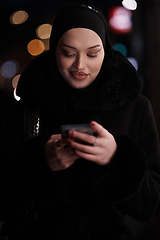 Image showing uropean Muslim Hijabi Business Lady checking her phone on urban city street at night