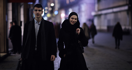 Image showing Happy multicultural business couple walking together outdoors in an urban city street at night near a jewelry shopping store window.