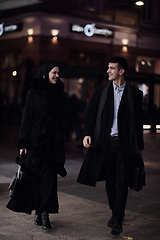 Image showing Happy multicultural business couple walking together outdoors in an urban city street at night near a jewelry shopping store window.