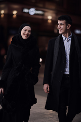 Image showing Happy multicultural business couple walking together outdoors in an urban city street at night near a jewelry shopping store window.