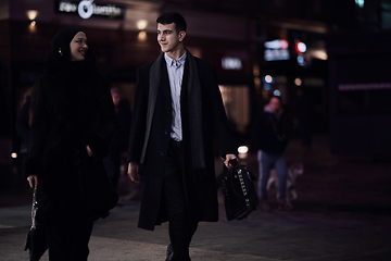 Image showing Happy multicultural business couple walking together outdoors in an urban city street at night near a jewelry shopping store window.