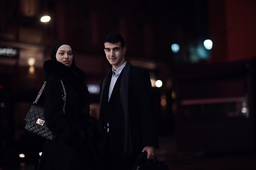 Image showing Happy multicultural business couple walking together outdoors in an urban city street at night near a jewelry shopping store window.