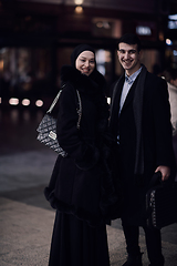 Image showing Happy multicultural business couple walking together outdoors in an urban city street at night near a jewelry shopping store window.