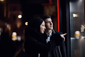 Image showing Happy multicultural business couple walking together outdoors in an urban city street at night near a jewelry shopping store window.