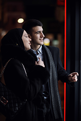 Image showing Happy multicultural business couple walking together outdoors in an urban city street at night near a jewelry shopping store window.