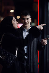 Image showing Happy multicultural business couple walking together outdoors in an urban city street at night near a jewelry shopping store window.