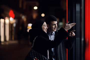 Image showing Happy multicultural business couple walking together outdoors in an urban city street at night near a jewelry shopping store window.