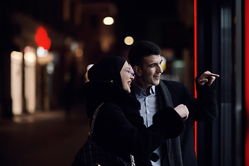 Image showing Happy multicultural business couple walking together outdoors in an urban city street at night near a jewelry shopping store window.