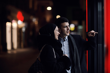 Image showing Happy multicultural business couple walking together outdoors in an urban city street at night near a jewelry shopping store window.