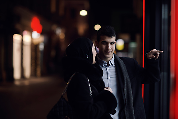 Image showing Happy multicultural business couple walking together outdoors in an urban city street at night near a jewelry shopping store window.