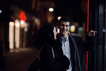 Image showing Happy multicultural business couple walking together outdoors in an urban city street at night near a jewelry shopping store window.