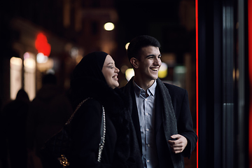 Image showing Happy multicultural business couple walking together outdoors in an urban city street at night near a jewelry shopping store window.