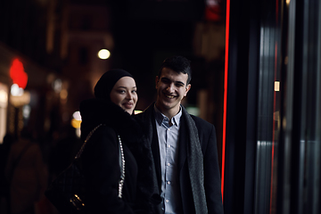 Image showing Happy multicultural business couple walking together outdoors in an urban city street at night near a jewelry shopping store window.