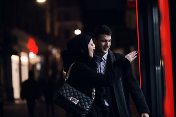 Image showing Happy multicultural business couple walking together outdoors in an urban city street at night near a jewelry shopping store window.