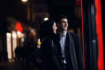 Image showing Happy multicultural business couple walking together outdoors in an urban city street at night near a jewelry shopping store window.