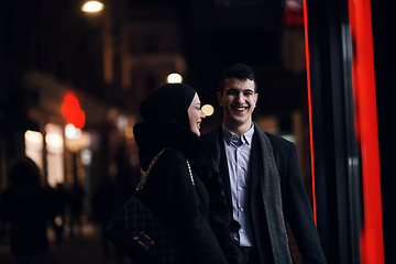 Image showing Happy multicultural business couple walking together outdoors in an urban city street at night near a jewelry shopping store window.