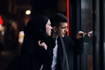 Image showing Happy multicultural business couple walking together outdoors in an urban city street at night near a jewelry shopping store window.