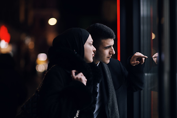 Image showing Happy multicultural business couple walking together outdoors in an urban city street at night near a jewelry shopping store window.