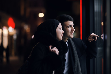 Image showing Happy multicultural business couple walking together outdoors in an urban city street at night near a jewelry shopping store window.