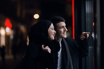 Image showing Happy multicultural business couple walking together outdoors in an urban city street at night near a jewelry shopping store window.