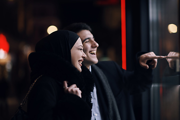 Image showing Happy multicultural business couple walking together outdoors in an urban city street at night near a jewelry shopping store window.