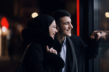 Image showing Happy multicultural business couple walking together outdoors in an urban city street at night near a jewelry shopping store window.