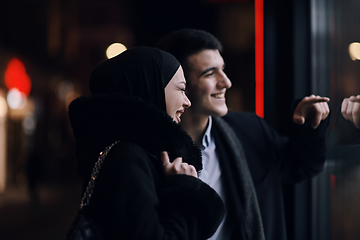 Image showing Happy multicultural business couple walking together outdoors in an urban city street at night near a jewelry shopping store window.