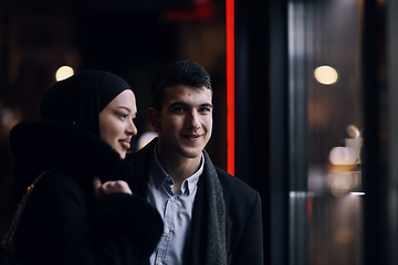 Image showing Happy multicultural business couple walking together outdoors in an urban city street at night near a jewelry shopping store window.