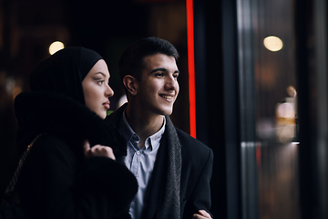 Image showing Happy multicultural business couple walking together outdoors in an urban city street at night near a jewelry shopping store window.