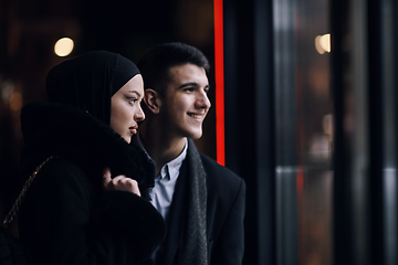 Image showing Happy multicultural business couple walking together outdoors in an urban city street at night near a jewelry shopping store window.