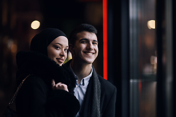 Image showing Happy multicultural business couple walking together outdoors in an urban city street at night near a jewelry shopping store window.