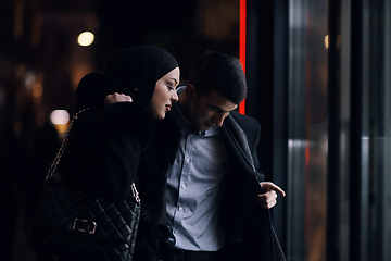 Image showing Happy multicultural business couple walking together outdoors in an urban city street at night near a jewelry shopping store window.