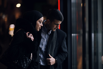 Image showing Happy multicultural business couple walking together outdoors in an urban city street at night near a jewelry shopping store window.