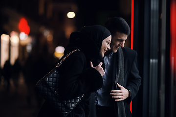 Image showing Happy multicultural business couple walking together outdoors in an urban city street at night near a jewelry shopping store window.