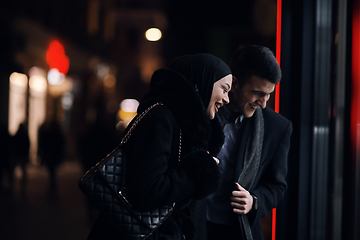 Image showing Happy multicultural business couple walking together outdoors in an urban city street at night near a jewelry shopping store window.