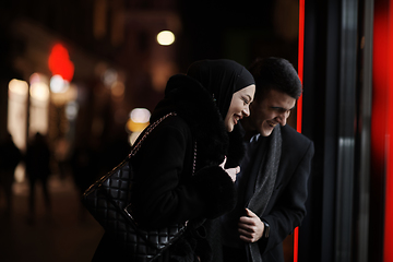 Image showing Happy multicultural business couple walking together outdoors in an urban city street at night near a jewelry shopping store window.