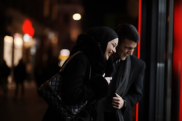 Image showing Happy multicultural business couple walking together outdoors in an urban city street at night near a jewelry shopping store window.