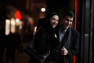 Image showing Happy multicultural business couple walking together outdoors in an urban city street at night near a jewelry shopping store window.