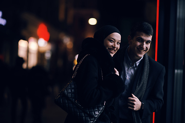 Image showing Happy multicultural business couple walking together outdoors in an urban city street at night near a jewelry shopping store window.