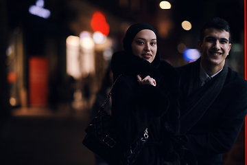 Image showing Happy multicultural business couple walking together outdoors in an urban city street at night near a jewelry shopping store window.