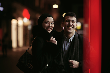 Image showing Happy multicultural business couple walking together outdoors in an urban city street at night near a jewelry shopping store window.