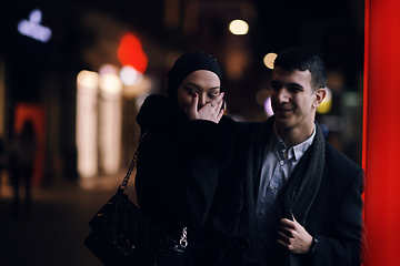 Image showing Happy multicultural business couple walking together outdoors in an urban city street at night near a jewelry shopping store window.