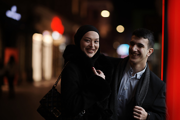 Image showing Happy multicultural business couple walking together outdoors in an urban city street at night near a jewelry shopping store window.