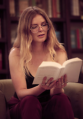 Image showing Reading, book and trendy woman in a library sitting on couch learning and relax in a bookstore or home. Content female with novel for knowledge, study and literature or fiction story