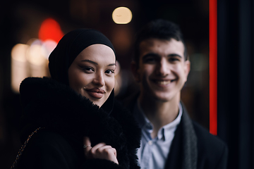 Image showing Happy multicultural business couple walking together outdoors in an urban city street at night near a jewelry shopping store window.