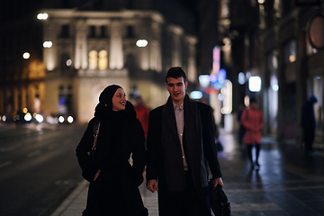 Image showing Happy multicultural business couple walking together outdoors in an urban city street at night near a jewelry shopping store window.