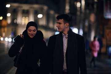 Image showing Happy multicultural business couple walking together outdoors in an urban city street at night near a jewelry shopping store window.