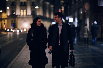 Image showing Happy multicultural business couple walking together outdoors in an urban city street at night near a jewelry shopping store window.