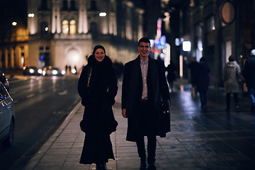 Image showing Happy multicultural business couple walking together outdoors in an urban city street at night near a jewelry shopping store window.